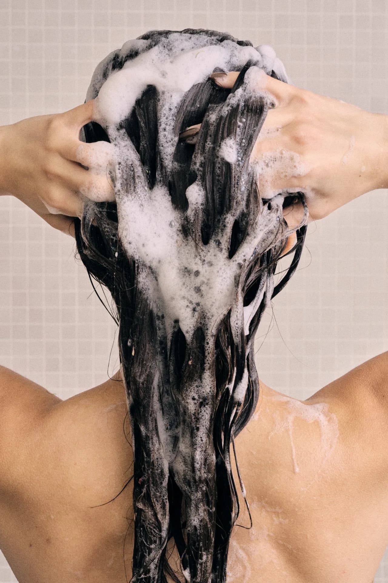 Mujer lavando su cabello con espuma, vista desde atrás